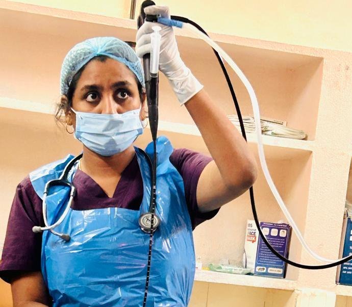 Dr. Pranathi in a theatre gown and mask, holding a flexible scope during an airway procedure